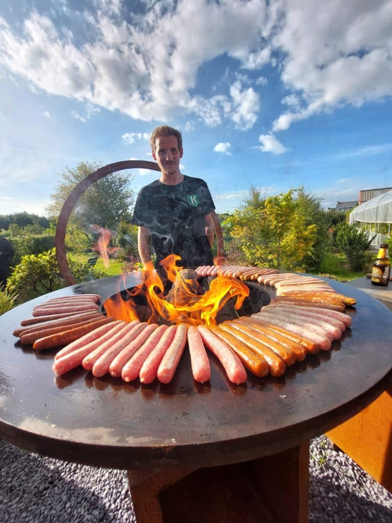 Quentin, gérant de l'entreprise, surveille la cuisson des saucisses, merguez sur le brasero OFYR lors de la soirée SKOL 2024.
