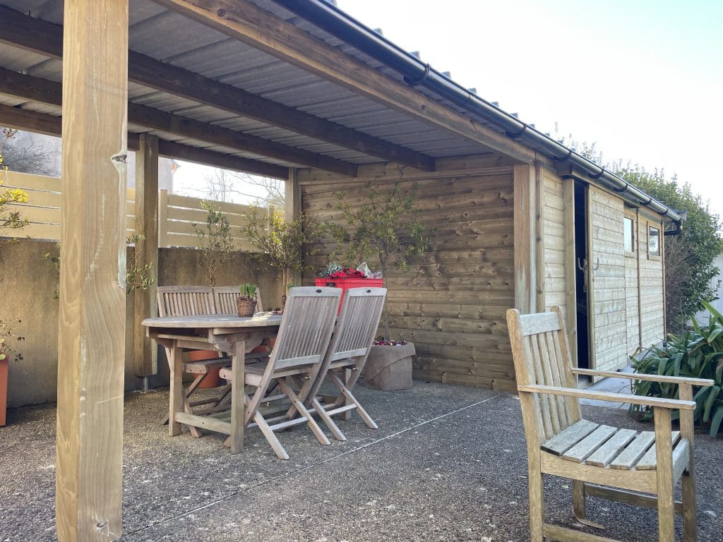 Abri en bois sur-mesure avec porte coulissante, double fenêtres et préau faisant office de terrasse